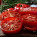 Sliced ripe tomatoes on a wooden surface, sprinkled with The Spice Lab Spanish Sea Salt Coarse Grain, while fresh rosemary and whole tomatoes are visible in the background. A ceramic grinder from The Spice Lab 3-Pack sits nearby.