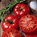 Sliced and whole tomatoes on a wooden board with The Spice Lab Spanish Sea Salt Coarse Grain from the 3-Pack Grinder, a sprig of rosemary, and a wooden spoon filled with coarse sea salt.