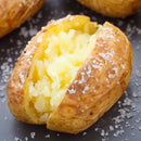 A baked potato split open, revealing fluffy yellow insides, topped with The Spice Lab Spanish Sea Salt Coarse Grain, freshly ground from the convenient 3-pack grinder.
