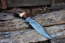 The Texan Knives Custom Handmade 13" Damascus Bowie Knife with a stag crown and rosewood handle plus leather sheath is displayed outdoors on weathered wooden planks.