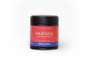 A 2.62 oz (74g) black jar of World Spice Harissa, featuring a red and blue label with the words "HARISSA HANDCRAFTED BLEND" from World Spice. This vibrant North African spice blend is described as Heat • Earthy • Picante, making it the perfect condiment for bringing authentic harissa flavor to your favorite dishes.