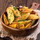 A wooden bowl filled with golden, crispy potato wedges is garnished with The Spice Lab Organic Whole Dill Weed, placed on a rustic wooden table with a frayed cloth underneath.
