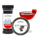 A container and tin of The Spice Lab Black Obsidian Salt Cocktail Rimmer are shown next to a red cocktail in a coupe glass, rimmed with Black Obsidian Salt and garnished with a strawberry.