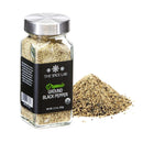 A glass jar from The Spice Lab Organic Starter Spice Set - 6 Jars sits next to a small pile of ground pepper. The jar, featuring a metal lid and sleek black label, is an essential addition to any organic spice collection for everyday cooking needs.