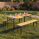 A 43.5 Inch Folding Kids Picnic Table & Bench Set No Assembly Wooden Toddler Table by DirectDeals sits on grass with colorful plates, cups, and snacks; a wooden fence and blooming bushes are in the background.