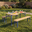 The 43.5 Inch Folding Kids Picnic Table & Bench Set No Assembly Wooden Toddler Table by DirectDeals sits on grass, holding colorful plates and snacks. Flowers, shrubs, and a wooden fence appear in the background.