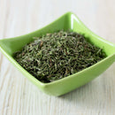 A green square bowl containing The Spice Lab Organic Whole Thyme by The Spice Lab sits on a light wooden surface, making it ideal for seasoning blends in French, Italian, and Mediterranean cuisine.