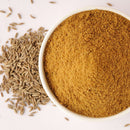 A white bowl filled with The Spice Lab Ground Cumin 1 lb Bulk Foodservice Spice sits next to a small pile of whole cumin seeds on a light surface.