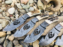 Four Texan Knives Deer Knives, each with a 10" wire-cut Damascus steel blade, antler horn handle, and leather sheath, are displayed on rocks. Artistic cutout animal designs and detailed etching give each knife a unique look.