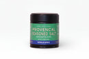 A black jar labeled World Spice Provencal Seasoned Salt, featuring a green and blue design, rests on a white background. This jar from World Spice contains 2.4 oz (68g) of sea salt infused with classic French flavor.