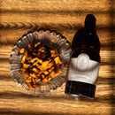 A glass bowl of roasted sweet potato cubes sits on a wooden surface beside a bottle of Under The Bark Syrup Co Cinnamon Maple Syrup, with sunlight highlighting the inviting pairing of the potatoes and this flavorful syrup.
