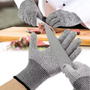 A person wearing gray NULU Safety Gloves from NULU Inc. slices meat on a wooden board with a knife, while another hand tests the gloves’ cut resistance by pressing a knife against them.