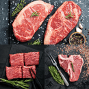 A mouthwatering spread from the Dude Food High Steaks Box by Dude Food showcases raw ribeye steaks, flavorful short ribs arranged with chopsticks, and a classic T-bone steak garnished with rosemary, peppercorns, garlic, and salt—featuring timeless favorites like T-Bones and Kansas City Strip Steaks.