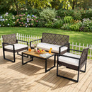 The DirectDeals 4-Piece Patio Conversation Set with Acacia Coffee Table includes two chairs, a loveseat, and a table topped with drinks, fruit, and pastries. White cushions, a white fence, and a flower garden complete the scene.