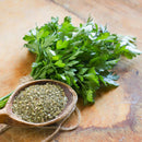A bunch of fresh parsley rests on a wooden surface beside a wooden spoon filled with The Spice Lab Organic Parsley Flakes, highlighting both fresh parsley and The Spice Lab’s dried parsley as perfect garnishing herbs.