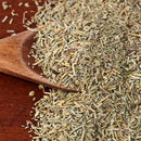 A wooden spoon filled with dried rosemary leaves, some spilling onto a wooden surface, evokes the essence of French and Mediterranean cuisine and pairs beautifully with The Spice Lab Organic Whole Thyme in your favorite seasoning blends.