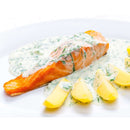 A cooked salmon fillet topped with a creamy dill sauce made using The Spice Lab Dill Weed Whole, served with sliced boiled potatoes and garnished with herbs on a white plate.