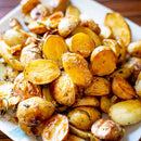 A plate of roasted baby potatoes, halved and golden brown, seasoned with herbs, The Spice Lab Organic Cut and Sifted Rosemary, and pepper, displayed on a white dish.