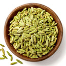 A wooden bowl filled with The Spice Lab Organic Fennel Seeds, known for their mild licorice flavor, with some scattered on a white surface nearby.