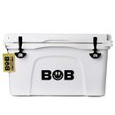 A white Bob The Cooler Co. 50 QT/47.3L Hard Cooler - El Amigo by Bob - The Cooler Co. with black latches and the BOB logo on the front, featuring a yellow tag labeled "BOB THE COOLER CO." hanging from the left latch. This sturdy, rectangular cooler offers extra thick insulated walls and includes a convenient removable dry basket inside.