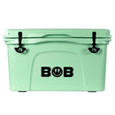 The Bob The Cooler Co. 50 QT/47.3L Hard Cooler - El Amigo by Bob - The Cooler Co. comes in mint green and features extra thick insulated walls, black latches, and a distinctive black BOB logo with a smiley face and lightning bolts at the center. It also includes a removable dry basket for added convenience.