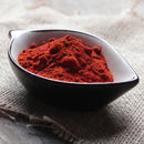 A black and white bowl filled with vibrant red The Spice Lab Smoked Spanish Paprika Powder sits on a piece of burlap fabric atop a wooden surface, ready to infuse bold flavor as a BBQ seasoning from The Spice Lab.