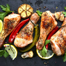 Roasted chicken drumsticks garnished with herbs, lemon slices, red and green chili peppers, fresh parsley, roasted garlic, and a sprinkling of freshly ground black pepper from The Spice Lab Premium Tellicherry Peppercorns with Grinder 3-Pack by The Spice Lab, all presented on a dark background.
