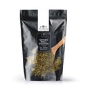 A black resealable pouch labeled The Spice Lab Red & Green Bell Pepper Flakes contains premium dried bell peppers, with a wooden spoon scooping colorful flakes and some scattered on a white surface. Perfect for bulk foodservice spices, the package displays the brand The Spice Lab and has a net weight of 1 lb.