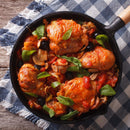 Chicken cacciatore with tomatoes, olives, mushrooms, and fresh basil—perfectly seasoned with The Spice Lab Organic Spanish Sweet Paprika—in a black skillet, resting on a blue and white checkered cloth atop a wooden table.
