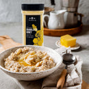 A bowl of oatmeal topped with The Spice Lab Granulated Honey and almond slices sits on a napkin with a spoon, accompanied by a container of The Spice Lab Granulated Honey, a slab of butter, and a teapot in the background—an inviting breakfast scene that showcases the versatility of this product from The Spice Lab for both home kitchens and bulk foodservice applications.
