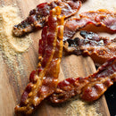Several crispy slices of glazed bacon are arranged on a wooden board, with scattered piles of The Spice Lab Maple Sugar Powder by The Spice Lab around them.