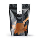 A black resealable bag labeled The Spice Lab Pumpkin Pie Spice, featuring an image of a wooden spoon with spice powder on the front. Ideal for fall baking, the package displays a net weight of 1 lb and showcases branding from The Spice Lab.