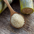 A wooden spoon holds The Spice Lab Turbinado Sugar, with sugarcane stalks and scattered sugar grains on a rustic wooden surface in the background, highlighting this less processed sugar from The Spice Lab—ideal for natural sweetening.
