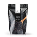 A black resealable bag labeled The Spice Lab Special Extra Bold Indian Black Peppercorns from The Spice Lab features a wooden spoon filled with extra bold peppercorns resting on top of the bag.