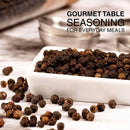 A white dish filled with whole organic black Tellicherry peppercorns from The Spice Lab rests on a marble surface, with a few peppercorns scattered nearby and text in the background that reads: “Gourmet Table Seasoning For Everyday Meals.” Perfect for pairing with The Spice Lab Himalayan Pink Salt Coarse in your favorite combo pack, The Spice Lab Himalayan Pink Salt Coarse & Organic Black Tellicherry Peppercorns Combo Pack.