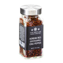 A clear glass jar with a silver lid holds The Spice Lab Korean Red Chili Pepper Flakes (Gochugaru), displaying a vibrant red color. The black label features the brand name, The Spice Lab, along with “Korean Red (Gochugaru) Chili Pepper.” The net weight is 1.8 oz (51g).
