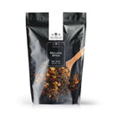 A black, resealable bag of The Spice Lab Mulling Spice (Net Wt. 1 lb) is shown with a wooden spoon scooping a fragrant blend of dried spices—ideal for making mulled wine or apple cider. The package features the brand name “The Spice Lab” prominently at the top.
