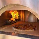 A pizza topped with chicken and red onion bakes on a stone surface inside the Traditional 25 Dual Fueled Outdoor Oven, with bright orange flames rising from the WPPO Gas Burner for Dual Fueled Outdoor Oven by WPPO LLC Direct at the back—perfect for elevating your outdoor cooking experience.