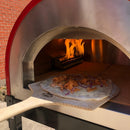 A pizza topped with shredded meat and red onions is being placed into a wood-fired oven on the WPPO 16" x 36" Long Handled Wooden Pizza Peel from WPPO LLC Direct, with flames visible inside the oven—a classic moment in traditional pizza making.