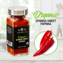 A jar of The Spice Lab Organic Spanish Sweet Paprika is placed beside two vibrant red sweet peppers on a white plate, highlighted by a bright kitchen backdrop and green text—making it an ideal ingredient from The Spice Lab for enhancing BBQ rubs or seasoning dishes with the authentic taste of Sweet Paprika Pimenton.