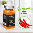 A jar of The Spice Lab Organic Chili Powder rests on a white surface beside three fresh red chili peppers, featuring the words “Organic Chili Powder” in green and black—ideal for infusing your favorite Mexican dishes with bold flavor or crafting spicy rubs.