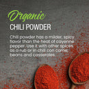 Two wooden spoons filled with The Spice Lab Organic Chili Powder rest on a gray surface, with extra chili powder sprinkled around. Text highlights The Spice Lab’s organic chili powder’s milder flavor and versatility, making it perfect for Mexican seasonings and spicy rubs.