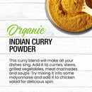A bowl of The Spice Lab Organic Indian Curry Powder rests on a white wood surface. Text beside it highlights this flavorful, organic seasoning from The Spice Lab and recommends adding it to curries, stews, grilled vegetables, meat dishes, or chicken salad.
