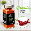 A glass jar labeled The Spice Lab Organic Cayenne Pepper sits on a kitchen counter, accompanied by two dried red cayenne peppers and the words “The Spice Lab Organic Cayenne Pepper” displayed alongside—an essential spice from The Spice Lab for adding bold heat to Mexican or Indian dishes.