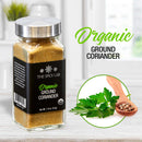 A jar of The Spice Lab Organic Ground Coriander is placed beside a wooden spoon filled with coriander seeds and fresh coriander leaves, emphasizing its key role in Indian cuisine. Text on the image reads “The Spice Lab Organic Ground Coriander,” making it ideal for elevating your favorite spice blends.