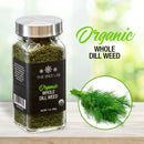 A glass jar of The Spice Lab Organic Whole Dill Weed sits next to a fresh bunch of dill on a wooden surface, perfect for enhancing dishes like tzatziki. The scene’s bright, blurred background highlights the freshness and premium quality of this organic dried dill from The Spice Lab.