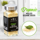 A glass jar labeled The Spice Lab Organic Hulled Sesame Seeds rests on a kitchen counter, ideal for infusing stir-fries or baked goods with a nutty flavor, while a circular inset features vibrant green sesame pods and seeds.