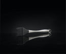 The Napoleon Grills Silicone Basting Brush with Stainless Steel Handle (55005) sits on a reflective black surface, its heat-resistant bristles and sleek design mirrored against the dark background.