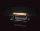 The Napoleon Cast Iron Chef's Press (56056) by Napoleon Grills, with a flat base and sturdy frame, features a wooden handle and is ideal for searing or pressing food evenly on the grill or stovetop.