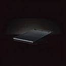 The Napoleon Grills Enameled Cast Iron Reversible Griddle for Rogue® 425 (56426), rectangular and black, is shown angled on a dark background with a subtle reflection beneath it.